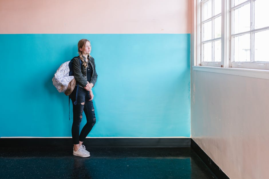 Teen student in casual attire with backpack looking out a window at school.